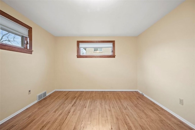 unfurnished room featuring a healthy amount of sunlight, visible vents, baseboards, and wood finished floors