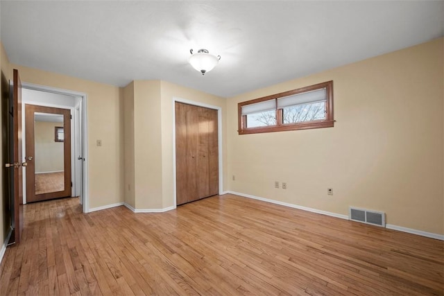 unfurnished bedroom featuring light wood-type flooring, a closet, visible vents, and baseboards