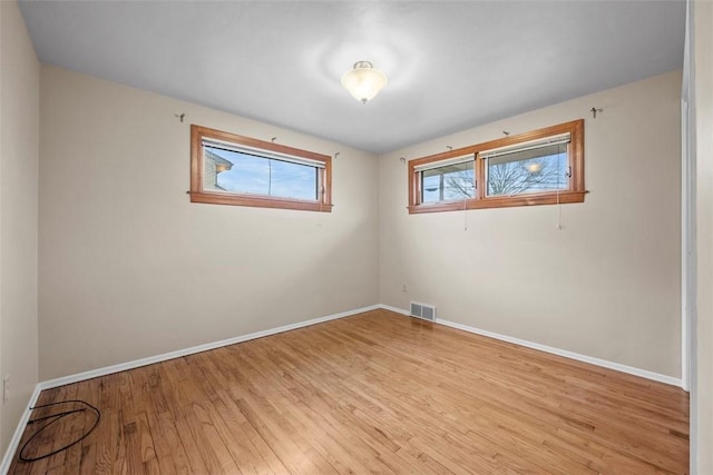 empty room with baseboards, visible vents, and light wood finished floors