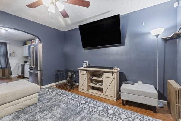 interior space with a ceiling fan, wood finished floors, arched walkways, radiator, and baseboards