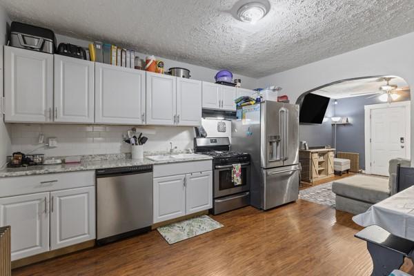 kitchen with arched walkways, stainless steel appliances, dark wood-type flooring, a ceiling fan, and a sink