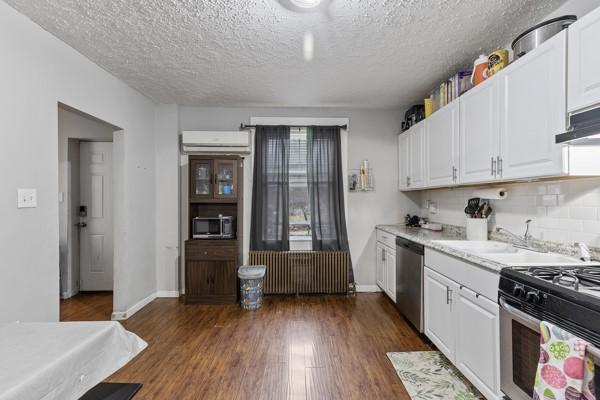 kitchen featuring dark wood-style flooring, a wall unit AC, radiator heating unit, appliances with stainless steel finishes, and white cabinetry