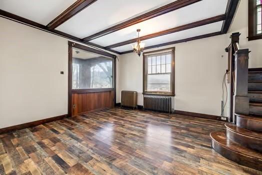 unfurnished living room featuring stairs, radiator heating unit, and wood finished floors