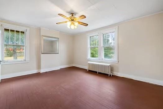 spare room with crown molding, radiator heating unit, wood finished floors, and baseboards