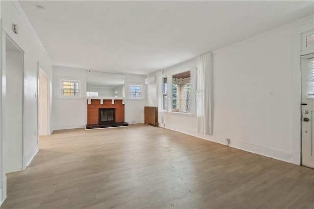 unfurnished living room featuring light wood finished floors, a fireplace, ornamental molding, and an AC wall unit