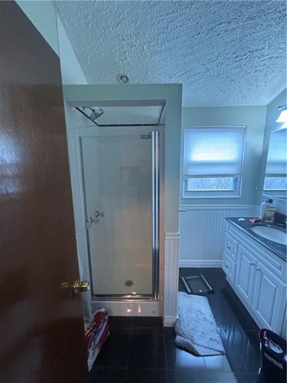 bathroom featuring a textured ceiling, tile patterned flooring, vanity, wainscoting, and a stall shower