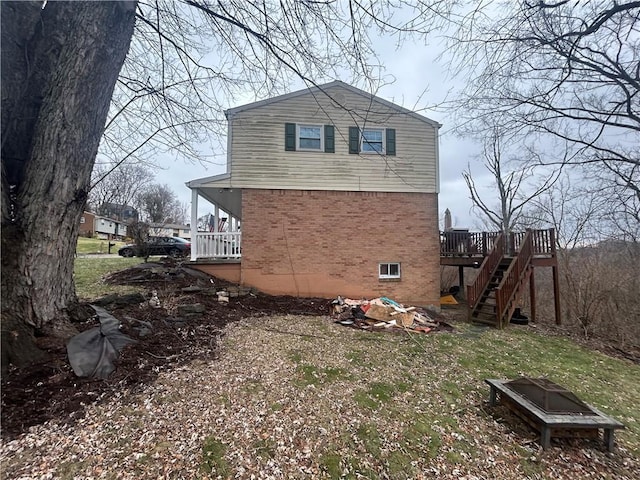 view of side of property featuring an outdoor fire pit, brick siding, a wooden deck, and stairs