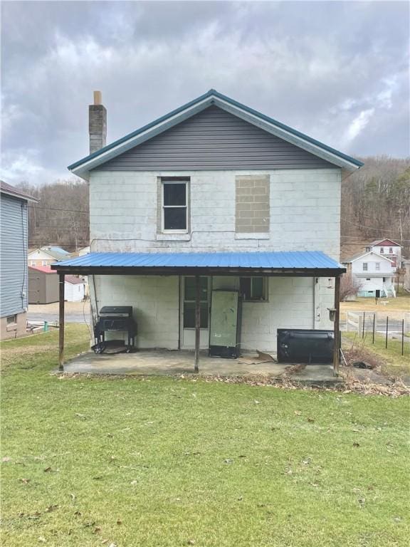 back of house with concrete block siding, a yard, a patio area, metal roof, and fence