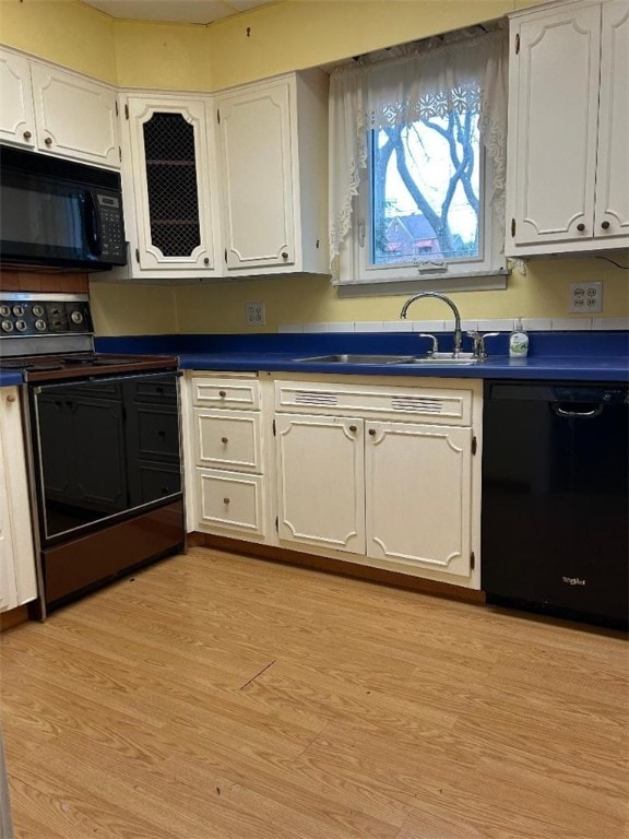 kitchen featuring dark countertops, white cabinetry, a sink, light wood-type flooring, and black appliances