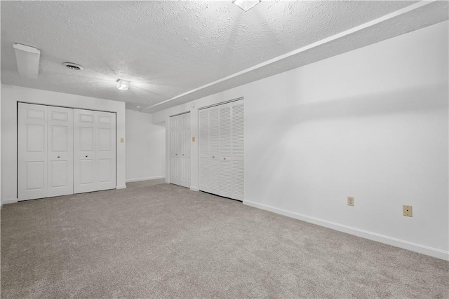 unfurnished bedroom with baseboards, visible vents, a textured ceiling, carpet floors, and two closets