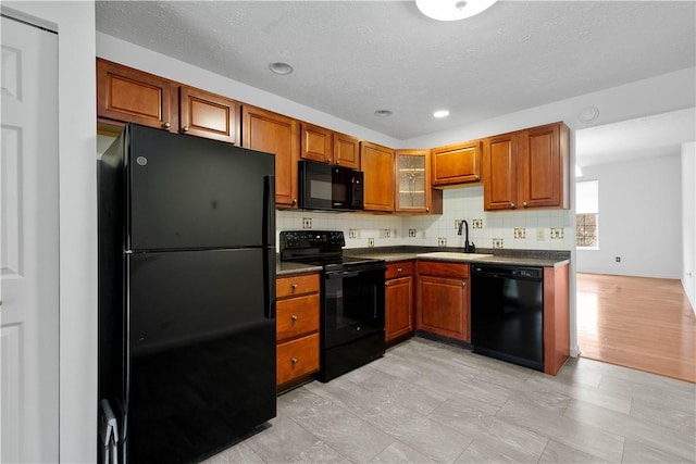 kitchen featuring a sink, backsplash, brown cabinets, black appliances, and dark countertops