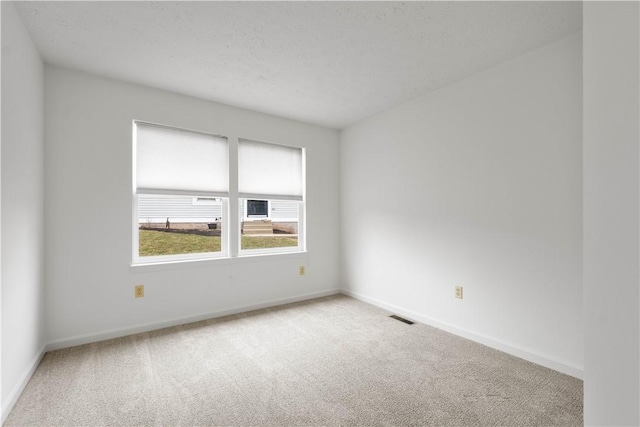 empty room with light colored carpet, visible vents, a textured ceiling, and baseboards