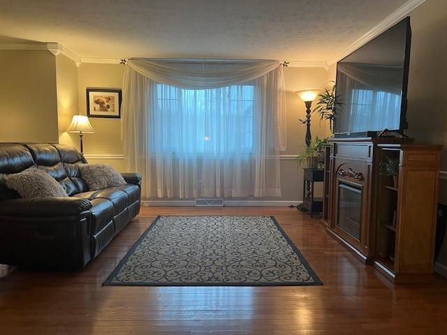 living room with a glass covered fireplace, ornamental molding, wood finished floors, and visible vents