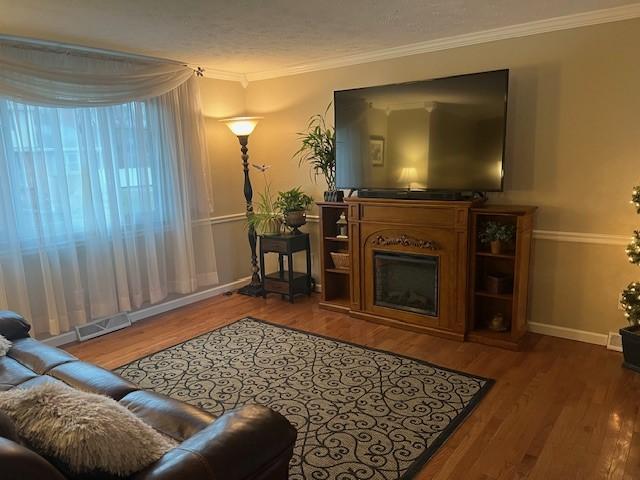 living room featuring crown molding, a fireplace, visible vents, and wood finished floors