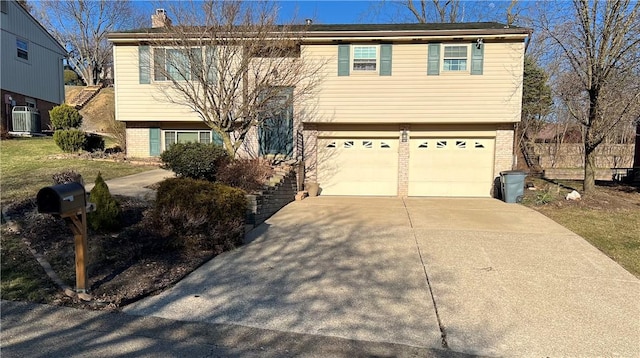 bi-level home featuring brick siding, concrete driveway, central AC, a chimney, and an attached garage