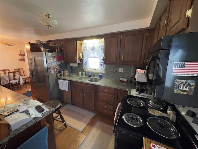 kitchen with light stone counters, backsplash, appliances with stainless steel finishes, light wood-style floors, and a sink