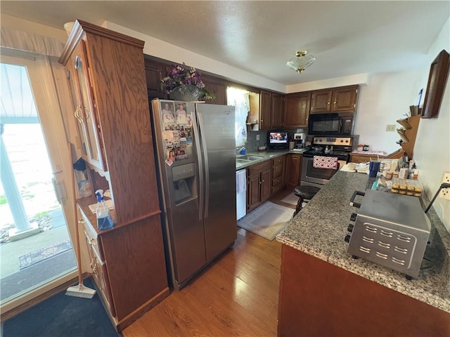 kitchen with stone counters, a sink, light wood-style floors, dark brown cabinets, and appliances with stainless steel finishes