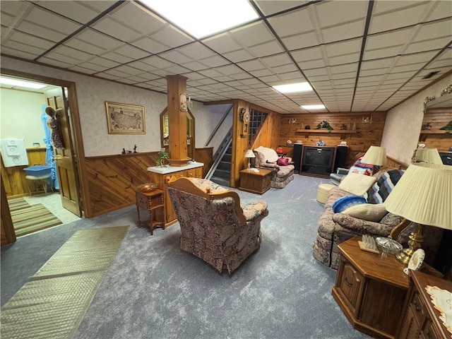 living room featuring stairway, a wainscoted wall, wooden walls, and a drop ceiling