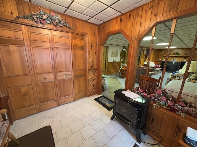 entrance foyer featuring a wood stove, light tile patterned floors, wooden walls, and arched walkways