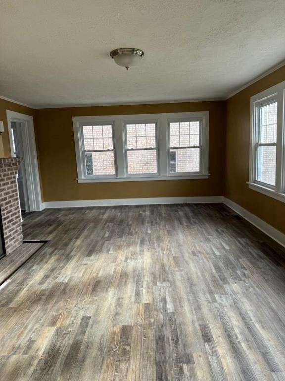 unfurnished living room featuring a textured ceiling, baseboards, a brick fireplace, dark wood finished floors, and crown molding