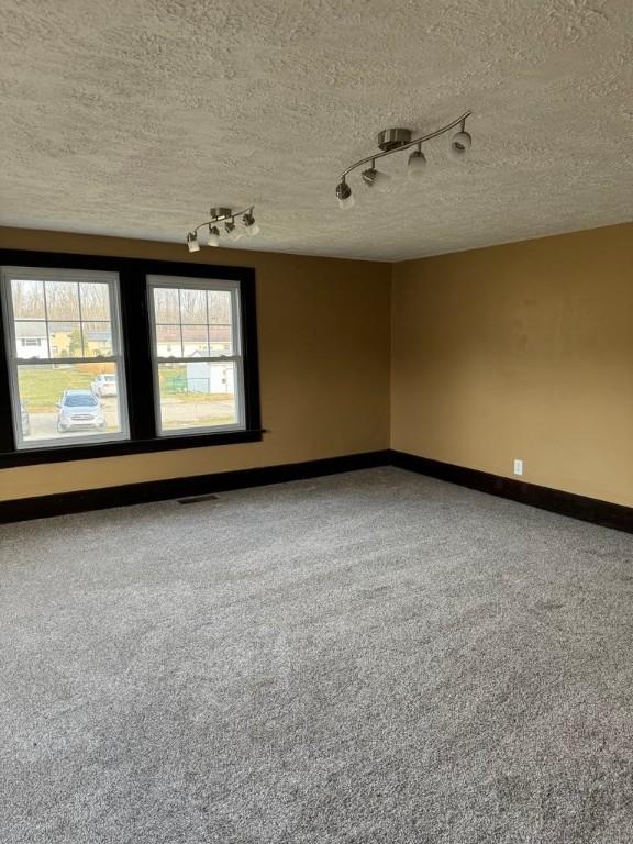 empty room featuring visible vents, a textured ceiling, and baseboards