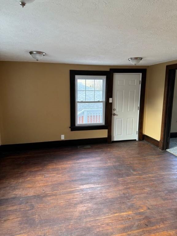 unfurnished room with a textured ceiling, dark wood-style flooring, visible vents, and baseboards