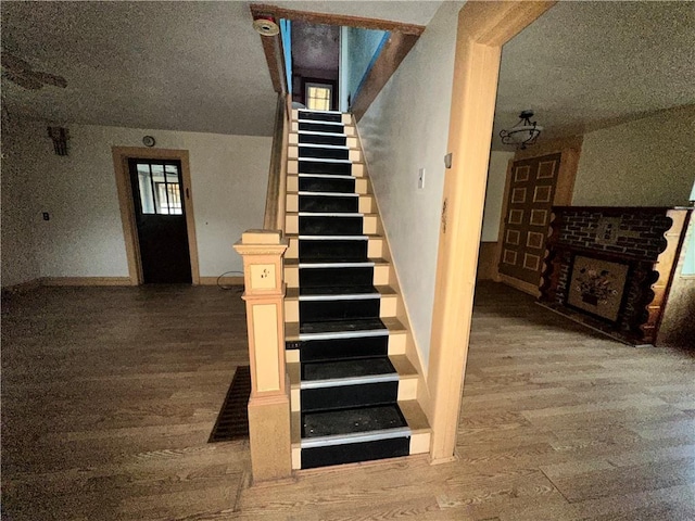 stairs with a brick fireplace, a textured ceiling, and wood finished floors