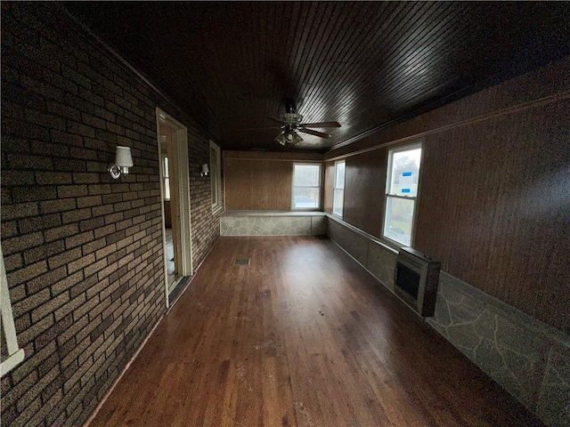 empty room with brick wall, wood finished floors, visible vents, a ceiling fan, and heating unit