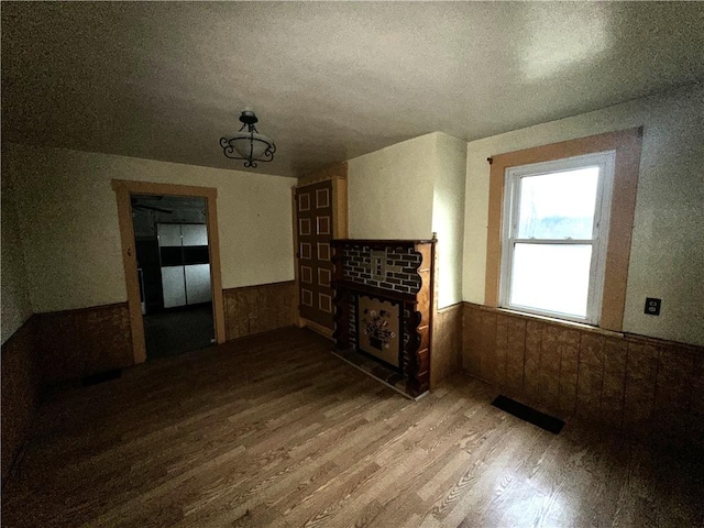 unfurnished living room featuring a fireplace, visible vents, wood finished floors, and wainscoting