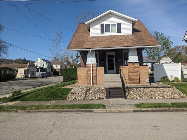 bungalow featuring a porch, brick siding, a shingled roof, and fence