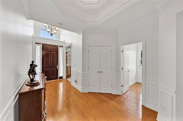 foyer entrance featuring wainscoting, crown molding, light wood-style flooring, and a decorative wall