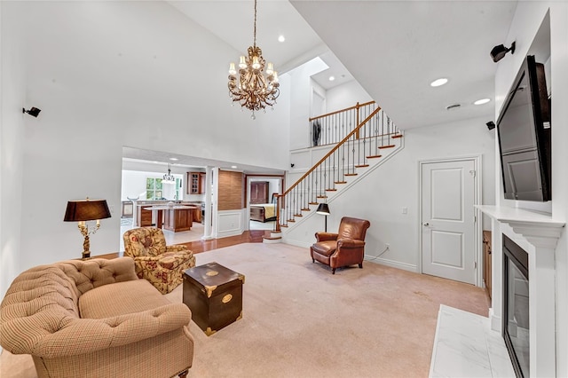 living area with a notable chandelier, light carpet, a fireplace with flush hearth, a towering ceiling, and stairs