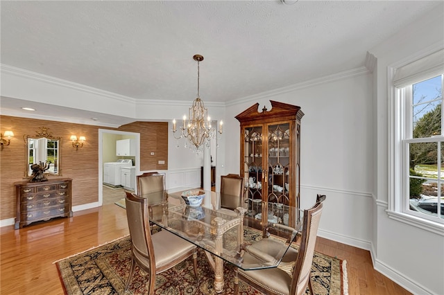 dining space with baseboards, ornamental molding, wood finished floors, washer and dryer, and a chandelier