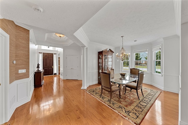 dining room featuring a textured ceiling, light wood-style floors, ornamental molding, ornate columns, and an inviting chandelier