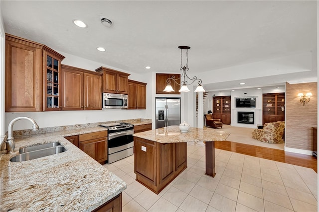 kitchen featuring a sink, open floor plan, appliances with stainless steel finishes, brown cabinetry, and a glass covered fireplace