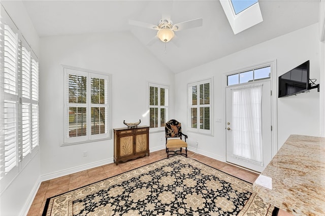 sitting room featuring a ceiling fan, vaulted ceiling with skylight, light tile patterned flooring, and baseboards