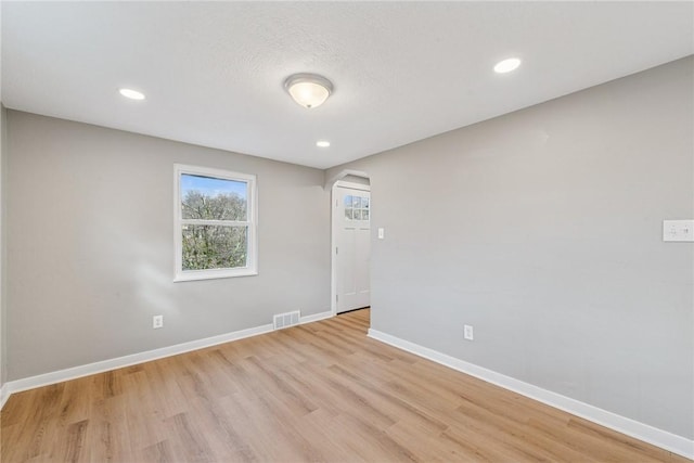 spare room with arched walkways, visible vents, light wood-style flooring, and baseboards