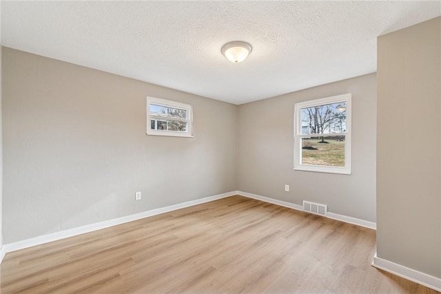 unfurnished room with light wood finished floors, a wealth of natural light, and visible vents