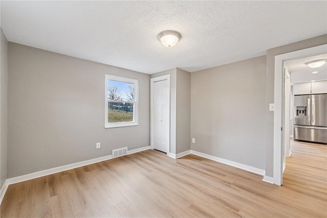 unfurnished bedroom featuring stainless steel fridge, visible vents, baseboards, light wood-style flooring, and a textured ceiling