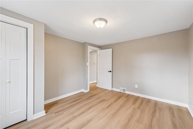 unfurnished bedroom featuring light wood-style floors, visible vents, a textured ceiling, and baseboards