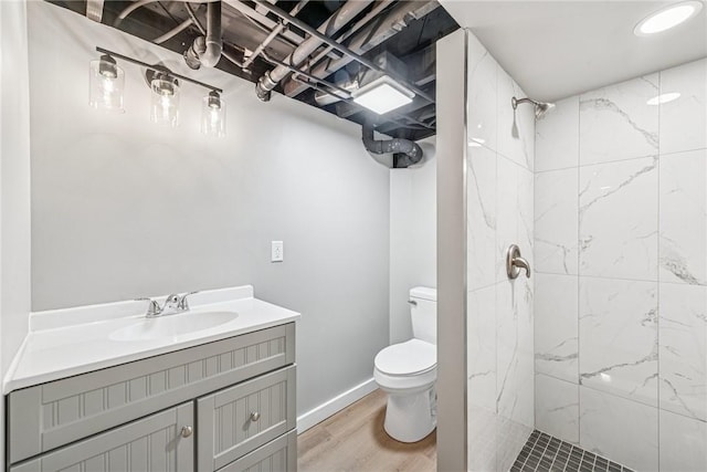 bathroom with baseboards, toilet, wood finished floors, a tile shower, and vanity