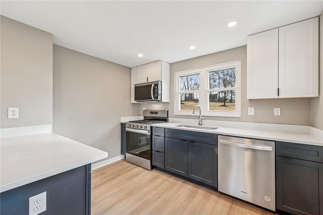 kitchen featuring stainless steel appliances, light countertops, light wood-style floors, white cabinetry, and a sink