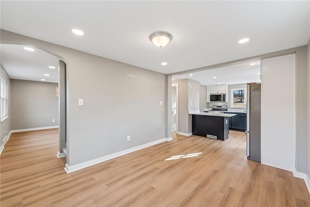 kitchen with arched walkways, light countertops, appliances with stainless steel finishes, light wood-style floors, and baseboards