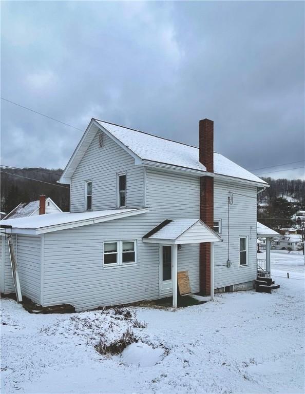 snow covered back of property with a chimney