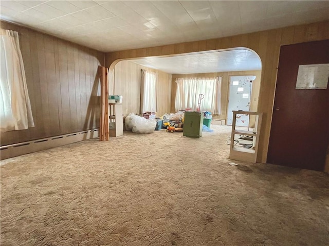 spare room featuring arched walkways, wood walls, a baseboard radiator, and carpet