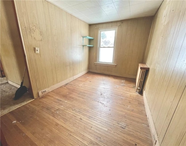 unfurnished room with baseboards, light wood-style floors, wood walls, and radiator