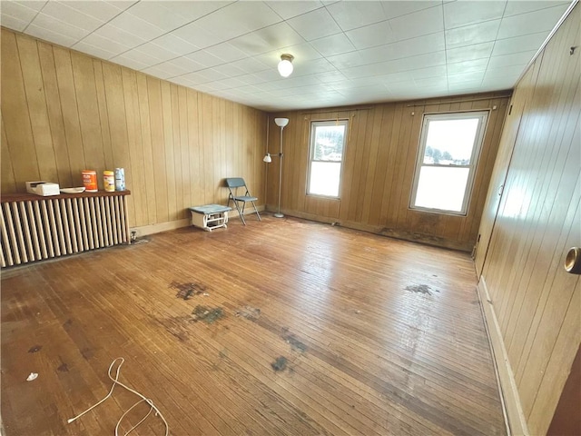 unfurnished room featuring radiator heating unit, baseboards, wooden walls, and hardwood / wood-style floors