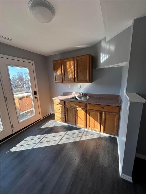 bar with dark wood-type flooring, a sink, and baseboards