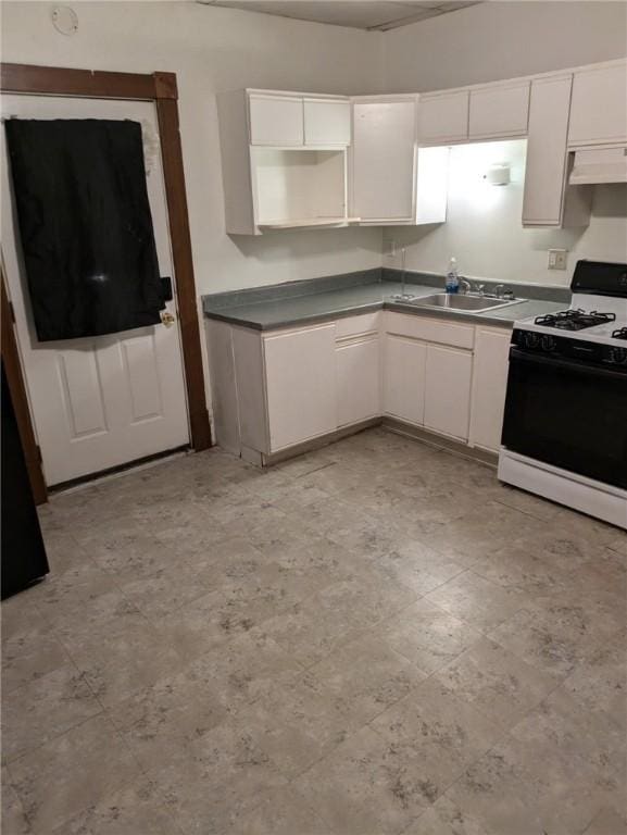 kitchen with dark countertops, white cabinetry, under cabinet range hood, and white gas range oven