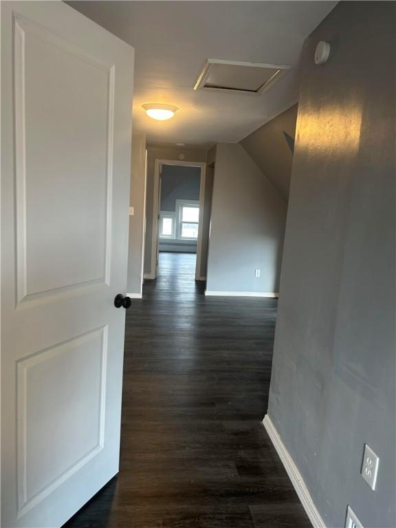 corridor featuring attic access, dark wood-style flooring, vaulted ceiling, and baseboards